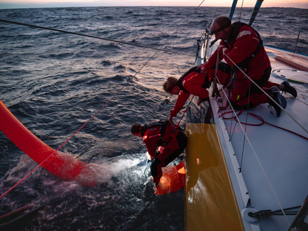 Malizia crew removing a net entangled on their foil in the middle of the ocean during The Ocean Race 2023.